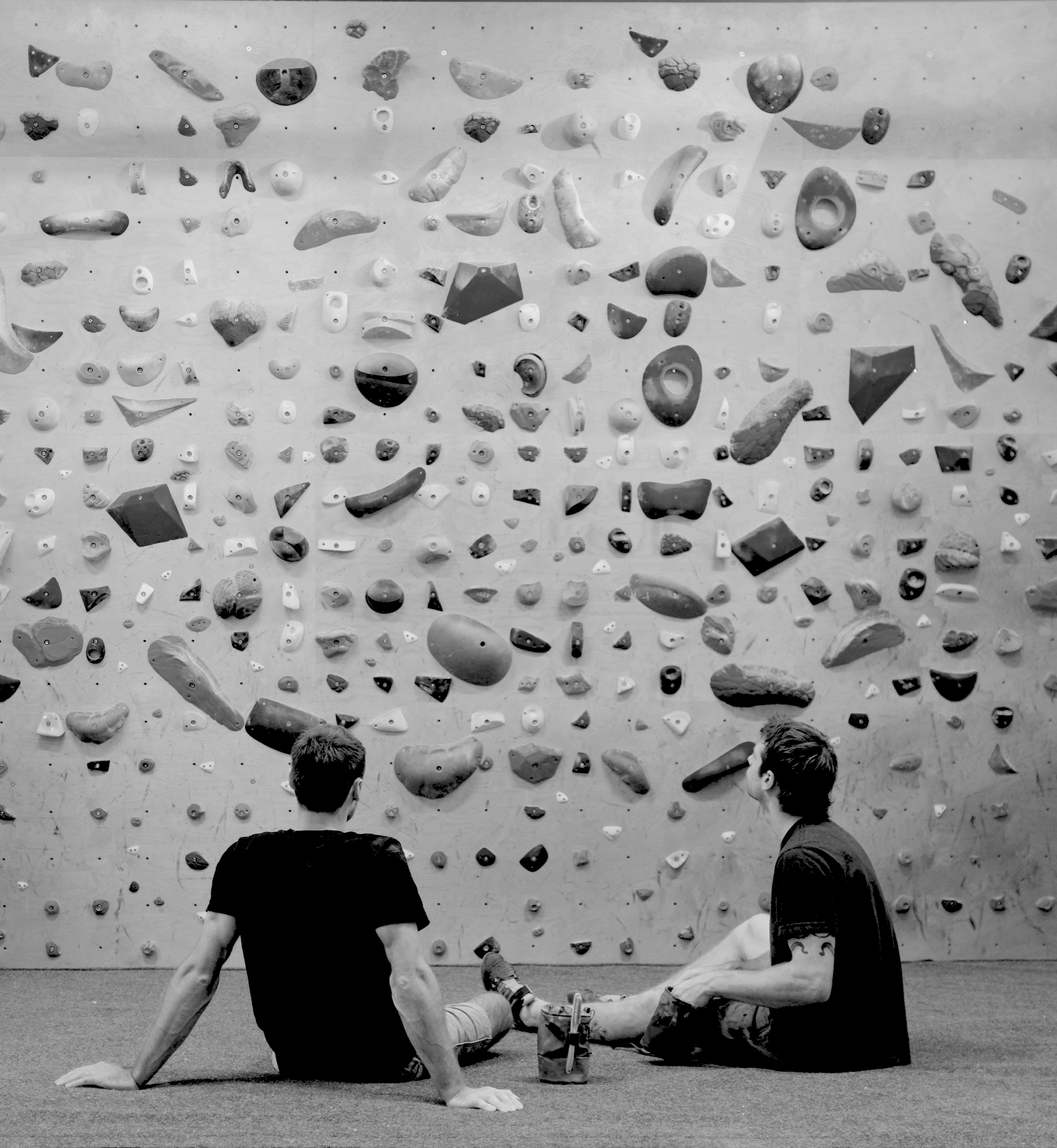 Two men sitting on the mat looking up at a bouldering wall